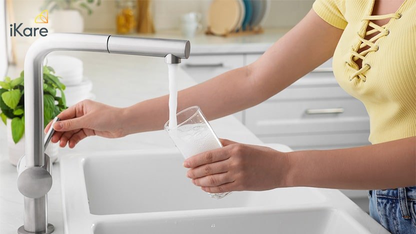 Image of a woman filling a glass with some tap water at the kitchen